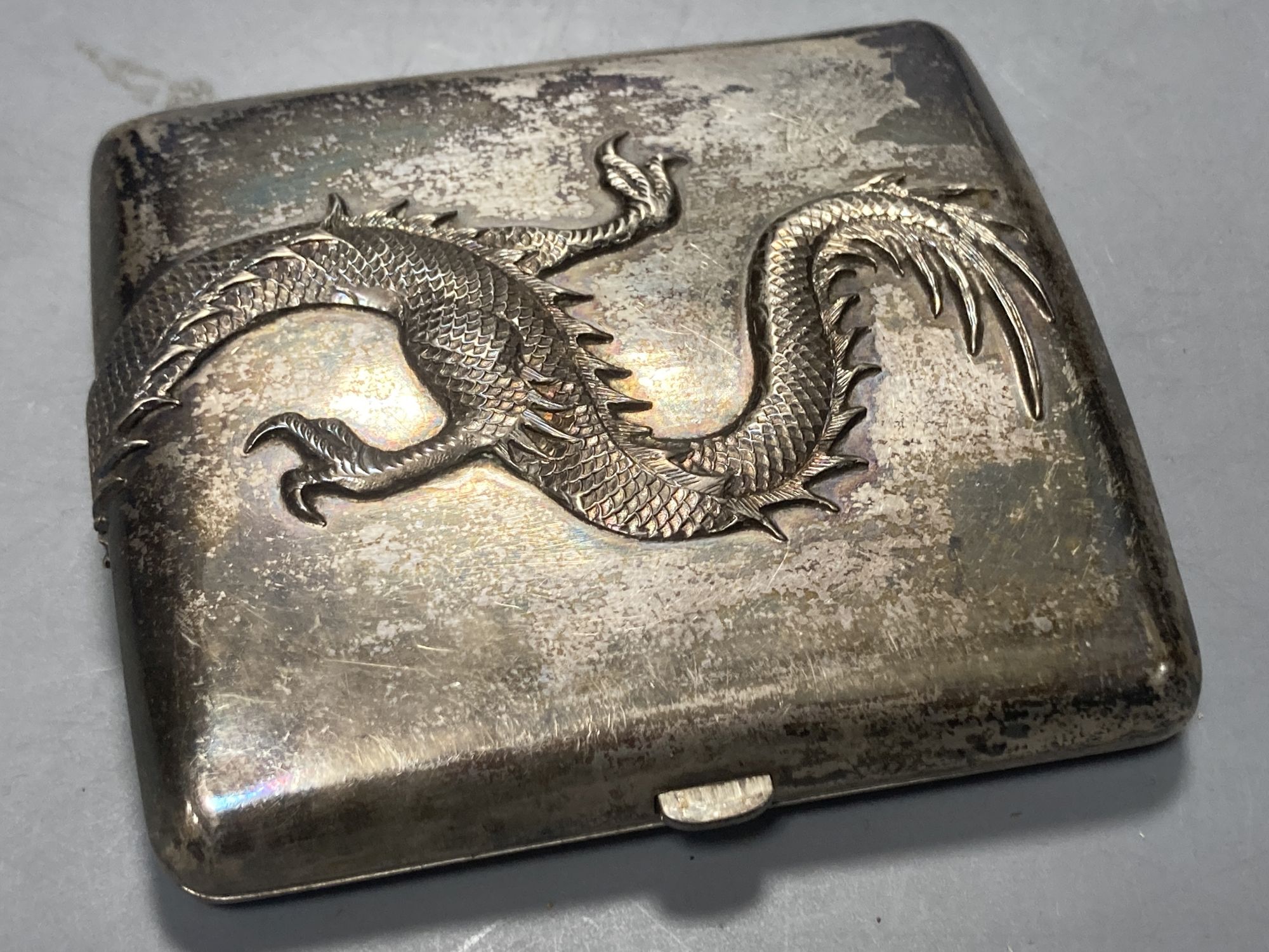A Chinese white metal cigarette case by Luen Hing, 75mm and four pairs of Chinese white metal belt buckles, three mounted on leather